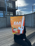 Trained by JP EAA 1 kg-påse, Orange & Mango-smak, hålls i handen